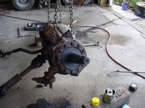 1992 Ford Bronco - A rusty heavy-duty steering axle hangs from lifting chains in a garage, showing the bolted third-member carrier, splined pinion shaft, knuc…