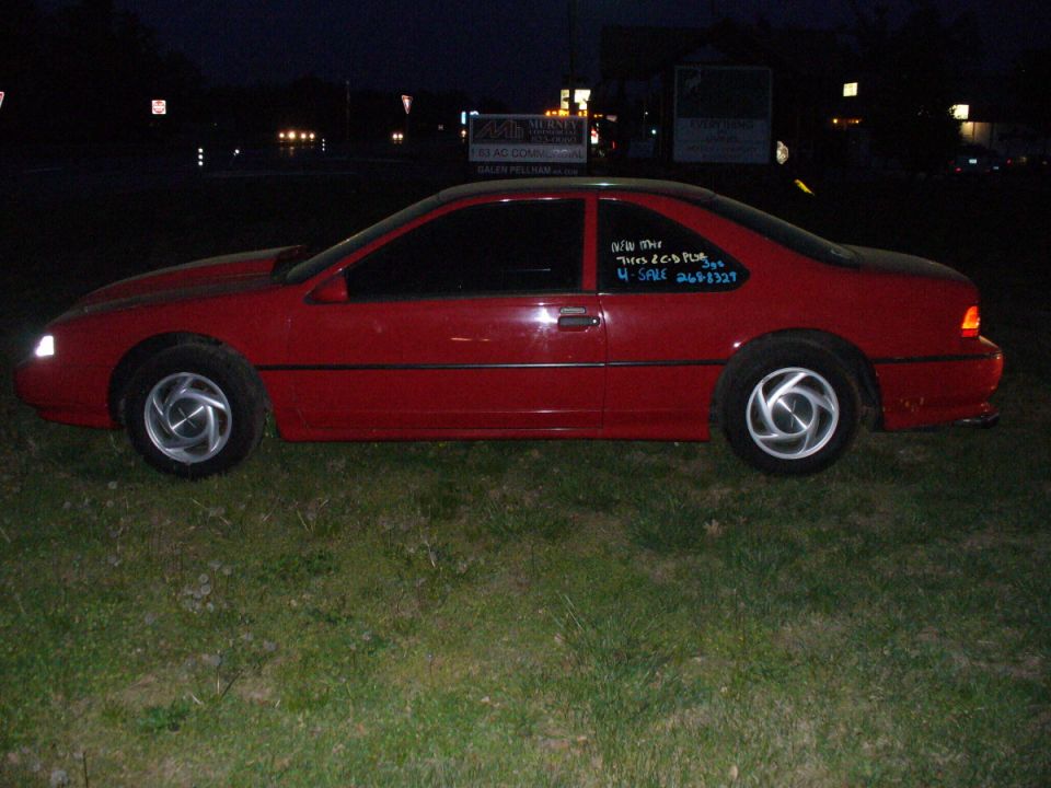 1995 Ford Thunderbird coupe, red, side view. Text on window reads 'NEW THUNDERBIRD 2.6 PLUG 4 SALE 269-8327'