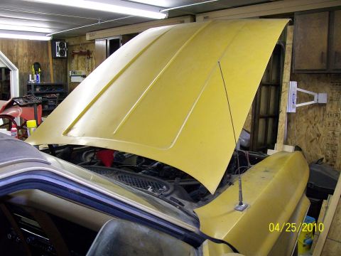 1972 Ford Mustang - A yellow car sits in a garage with its hood open, revealing the engine compartment.