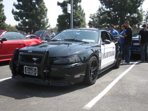 1990 Ford Probe - A modified Ford Mustang with police markings is parked in a lot next to other vehicles.