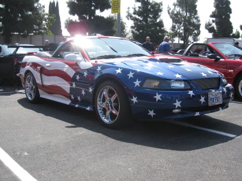 1990 Ford Probe - A convertible sports car is seen with an American flag paint scheme, parked next to another vehicle.