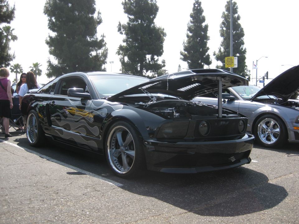 Black Ford Mustang with flame decals and hood open, parked next to a silver car