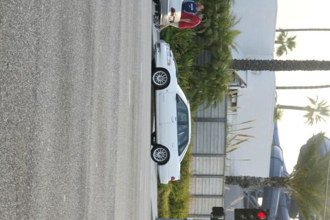 1992 Ford Taurus - A white sedan is parked on the side of the road with people standing near the rear of the vehicle.