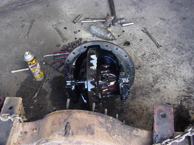 Open differential housing with ring-and-pinion gears on a shop floor surrounded by tools and a spray can