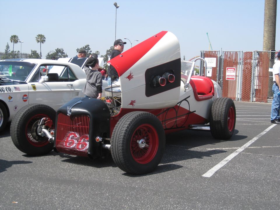 Red and white hot rod with number 66 on the front grille, parked next to a white car