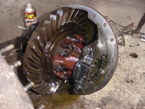 1992 Ford Bronco - Disassembled heavy-duty axle housing sitting on a shop floor with the cover off, exposing the oil-soaked hypoid ring gear, the red-painted…