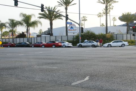 1992 Ford Taurus - A row of cars are parked along the street, with a building and palm trees visible behind them.