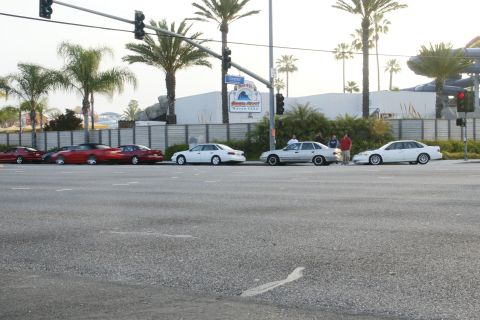 1992 Ford Taurus - A line of cars, including red coupes and white sedans, are parked along a street with a water park in the background.