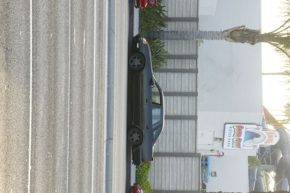 dark sedan parked in a lot, Knotts Soak City water park sign in background
