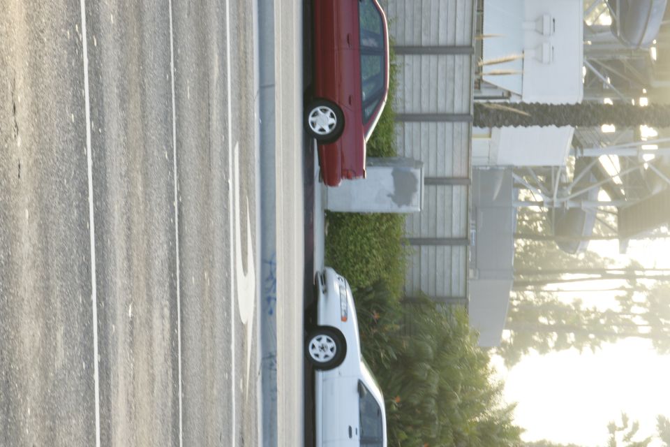 Red sedan and white van parked side-by-side on a street with a concrete barrier and fence