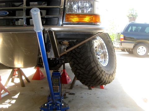 1996 Ford Bronco - A Ford truck's front suspension is elevated on jack stands for maintenance, with a custom bumper and large tire visible.