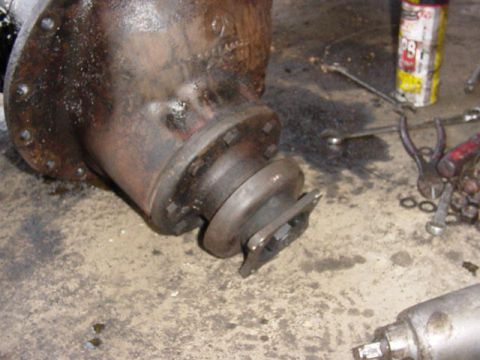 1992 Ford Bronco - A heavy cast axle differential housing lies on a concrete shop floor mid-teardown, its bolted cover flange and pinion yoke flange exposed w…