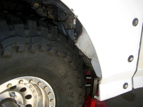 1996 Ford Bronco - Close-up view of the wheel well and tire of a white vehicle, with visible wiring and a red jack supporting it.