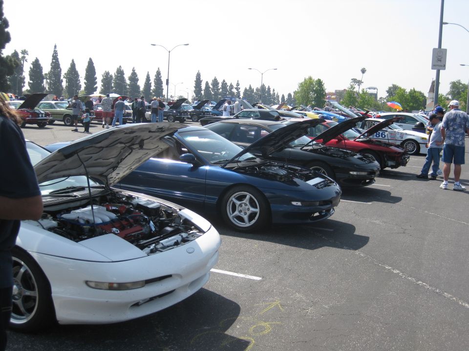 White Ford Probe with hood open, showing engine. Other cars parked in lot