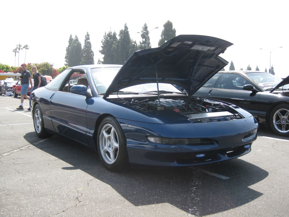 Blue coupe with hood open, showing engine bay. Silver wheels, dark tint. Parked outdoors