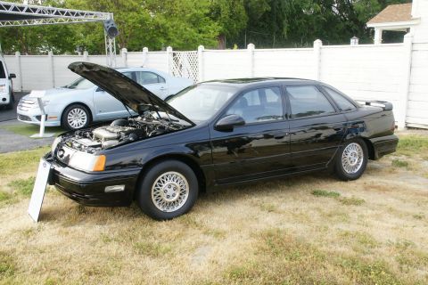 1992 Ford Taurus - A black 1992 Ford Taurus is displayed with its hood open, alongside another vehicle.
