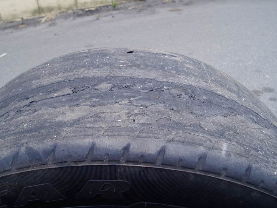 Tire with severely worn tread and visible damage, showing part of the sidewall with text