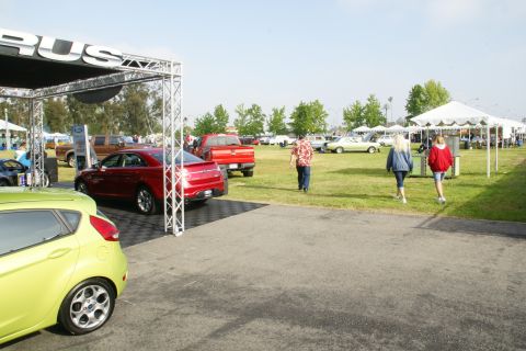 1992 Ford Taurus - A red sedan is viewed from the rear, parked under a tent at an outdoor car show with other vehicles and tents in the background.