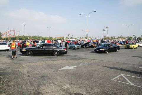 1992 Ford Taurus - A black Ford Crown Victoria is seen at a car show event with many other cars and attendees.