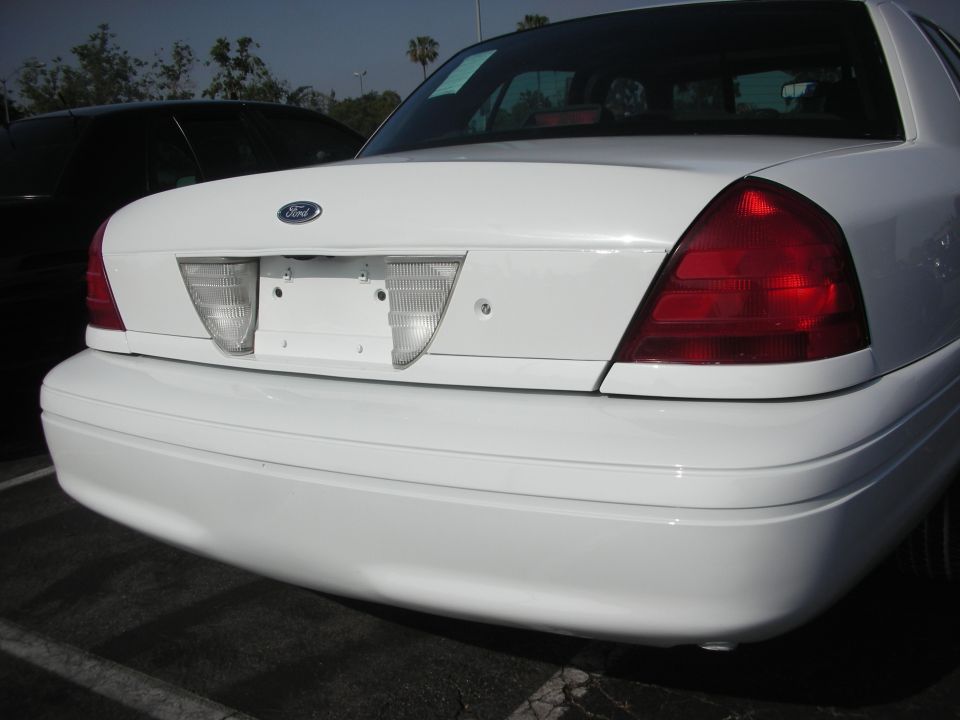 White Ford Crown Victoria rear bumper, taillights, and Ford emblem. Black car in background