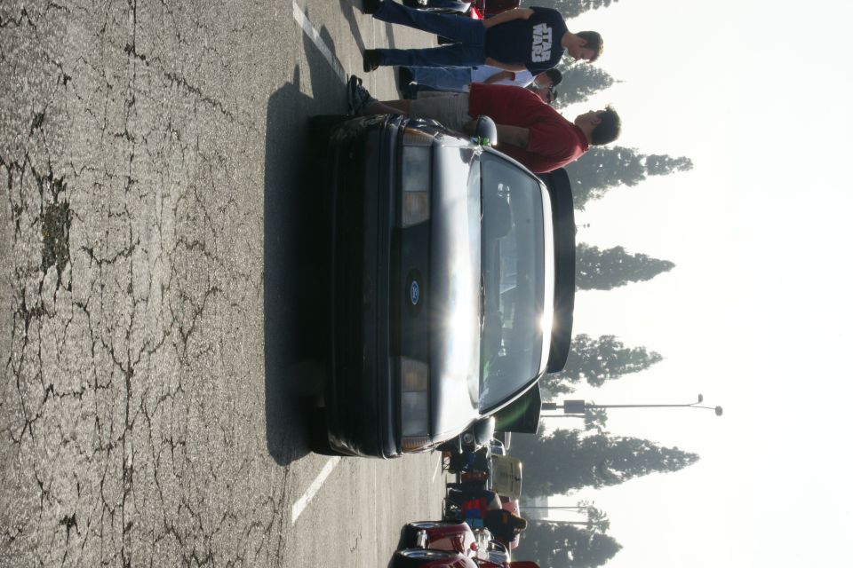 Front view of a 1992 Ford Taurus parked on cracked asphalt with people standing around it