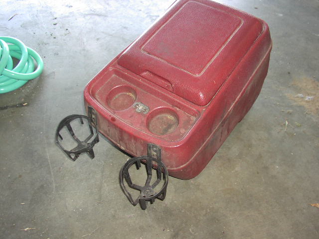Removed red plastic center console with cup holders sitting on a garage floor