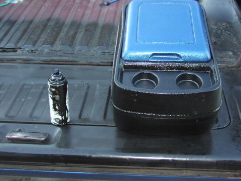 1981 Ford Bronco - A blue console with cup holders sits next to a can of spray paint on the bed of a pickup truck.