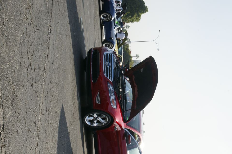Red Ford sedan with hood open, parked on cracked asphalt. Chrome wheels visible