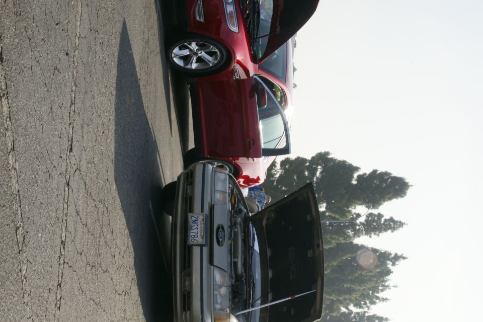 older gray Ford sedan with hood open, newer red Ford sedan parked next to it with door open