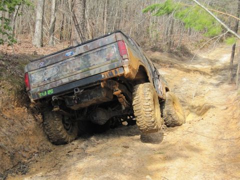 1993 Ford Bronco - This camouflaged Ford Bronco navigates a challenging muddy incline on a wooded trail.