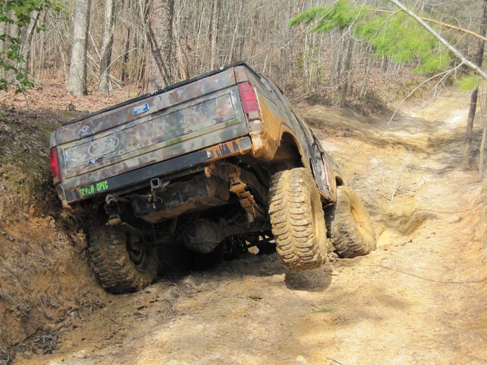 Camouflaged Ford Bronco on a muddy trail, rear view, with off-road tires and suspension visible