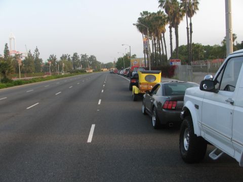 1996 Ford C-350 (Centurion Conversions) - A line of vehicles is parked along a highway, with palm trees and buildings visible in the distance.