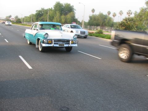 1996 Ford C-350 (Centurion Conversions) - A vintage two-tone coupe cruises down the highway alongside other vehicles.