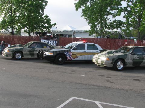 1996 Ford C-350 (Centurion Conversions) - Three vehicles, two modified Mustangs and a police car, are lined up with camouflage paint schemes and visible text.