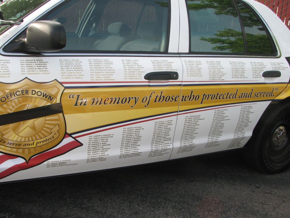 Side view of a white police car with "Officer Down" and "In memory of those who protected and served" text