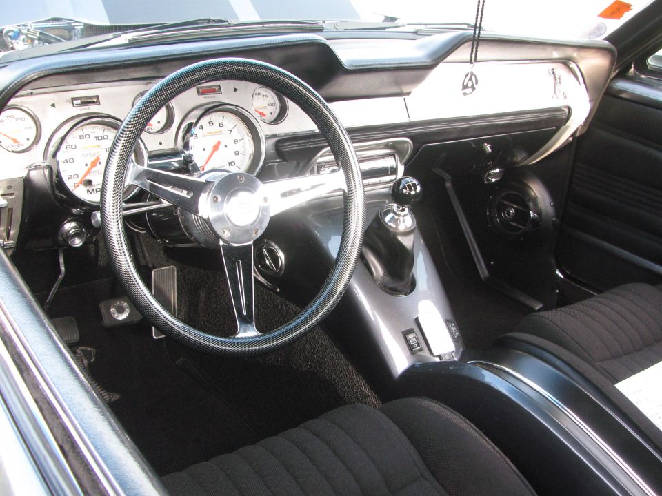 Custom car interior showing aftermarket gauges, a chrome steering wheel, and a shifter. The dashboard has a black finish