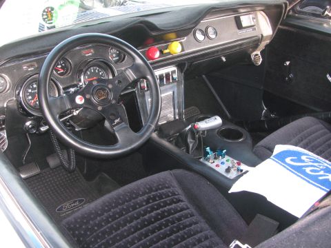 1996 Ford C-350 (Centurion Conversions) - The interior of a modified car features a GT steering wheel, custom shifter, and racing gauges, with a Ford towel on the seat.