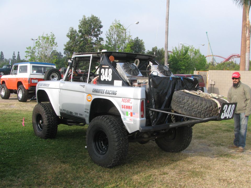 Silver modified Ford Bronco with number 348, spare tire on rear, and two fans visible