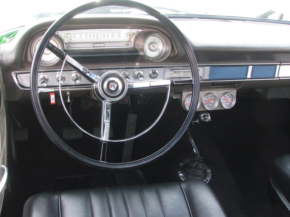 Car interior with a large steering wheel, dashboard gauges, and black seats. A red tag is visible on the steering column