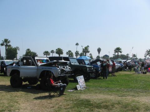 1996 Ford C-350 (Centurion Conversions) - A gathering of off-road vehicles displayed on a grassy field with palm trees in the background.
