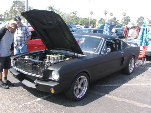 1996 Ford C-350 (Centurion Conversions) - A matte black 1967 Ford Mustang coupe is displayed with its hood open, revealing a custom engine and racing seats.