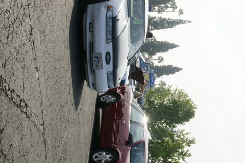 1992 Ford Taurus - A white 1992 Ford Taurus is parked next to a red car, with trees and a bright sky in the background.