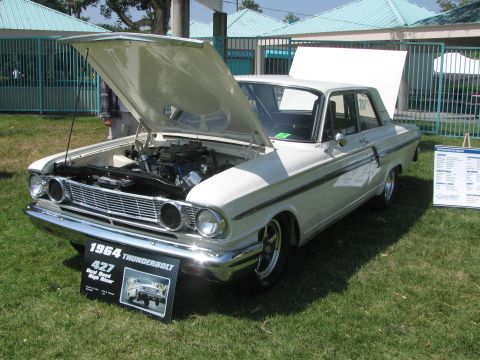 1996 Ford C-350 (Centurion Conversions) - A white 1964 Ford Thunderbolt is displayed with its hood open, revealing the engine and a sign detailing its 427 Dual Quad High Riser speci…