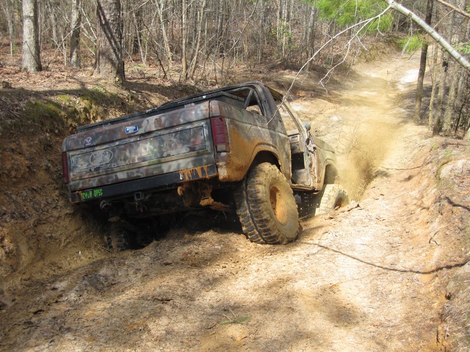 Muddy Ford Bronco climbing a dirt trail, tires kicking up dirt