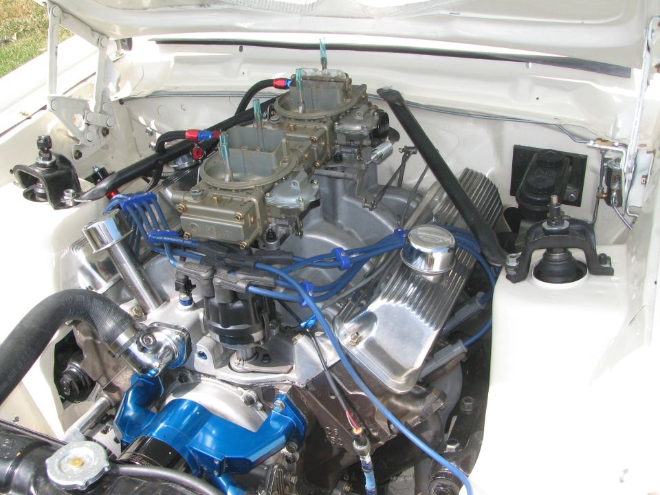 White vehicle engine bay with dual carburetors, chrome valve covers, and blue spark plug wires