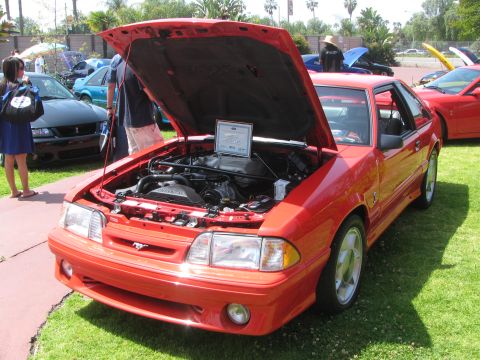 1996 Ford C-350 (Centurion Conversions) - Red Ford Mustang at an outdoor car show. The engine bay is open for display.