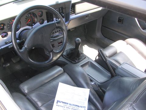 1996 Ford C-350 (Centurion Conversions) - The interior of a vehicle shows leather seats, a steering wheel, and a manual shifter, with a document on the passenger seat.