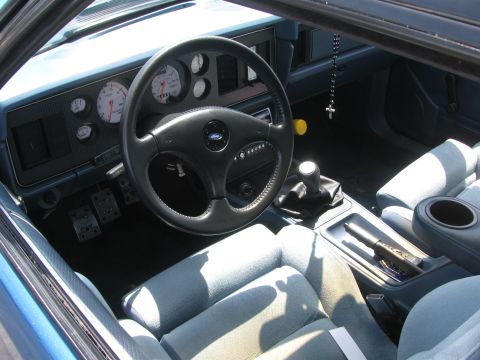1996 Ford C-350 (Centurion Conversions) - The interior of a car features light blue seats, a dashboard with gauges, and a manual transmission.