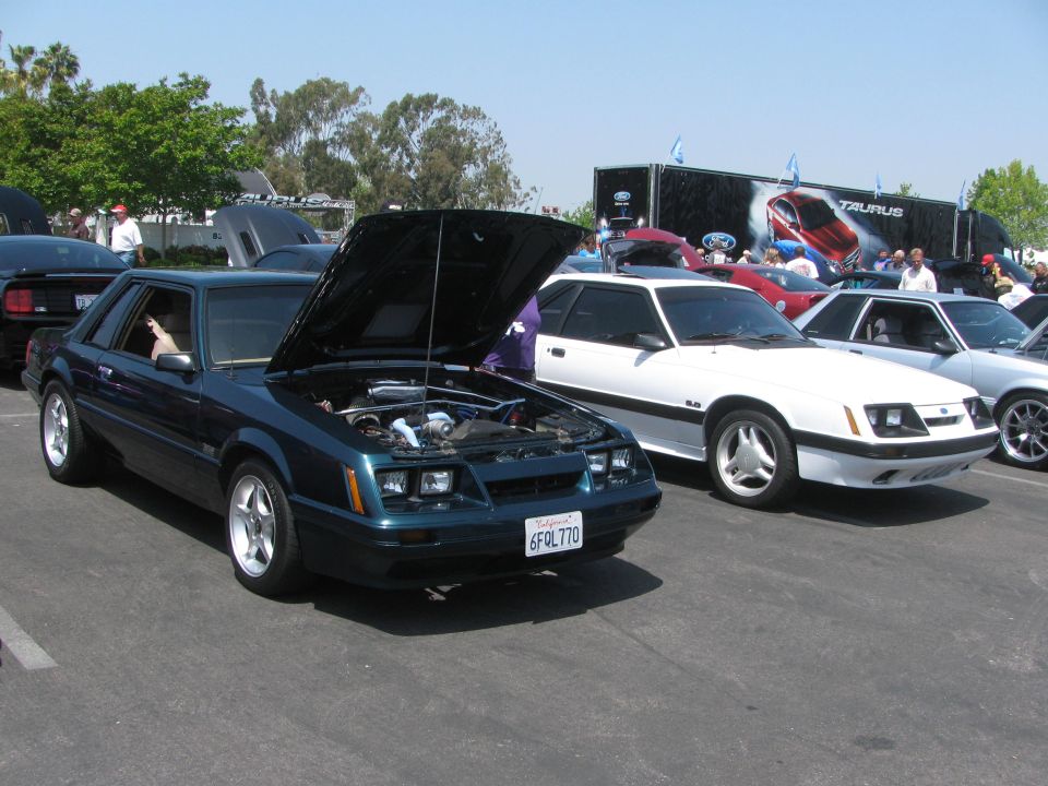 Dark teal Ford Mustang coupe with hood open, showing engine. California license plate 6FQL770. White Mustang parked to the right