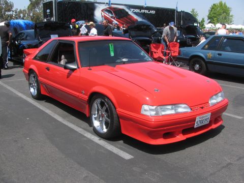 1996 Ford C-350 (Centurion Conversions) - Red coupe with aftermarket wheels and a hood scoop parked at an outdoor event.
